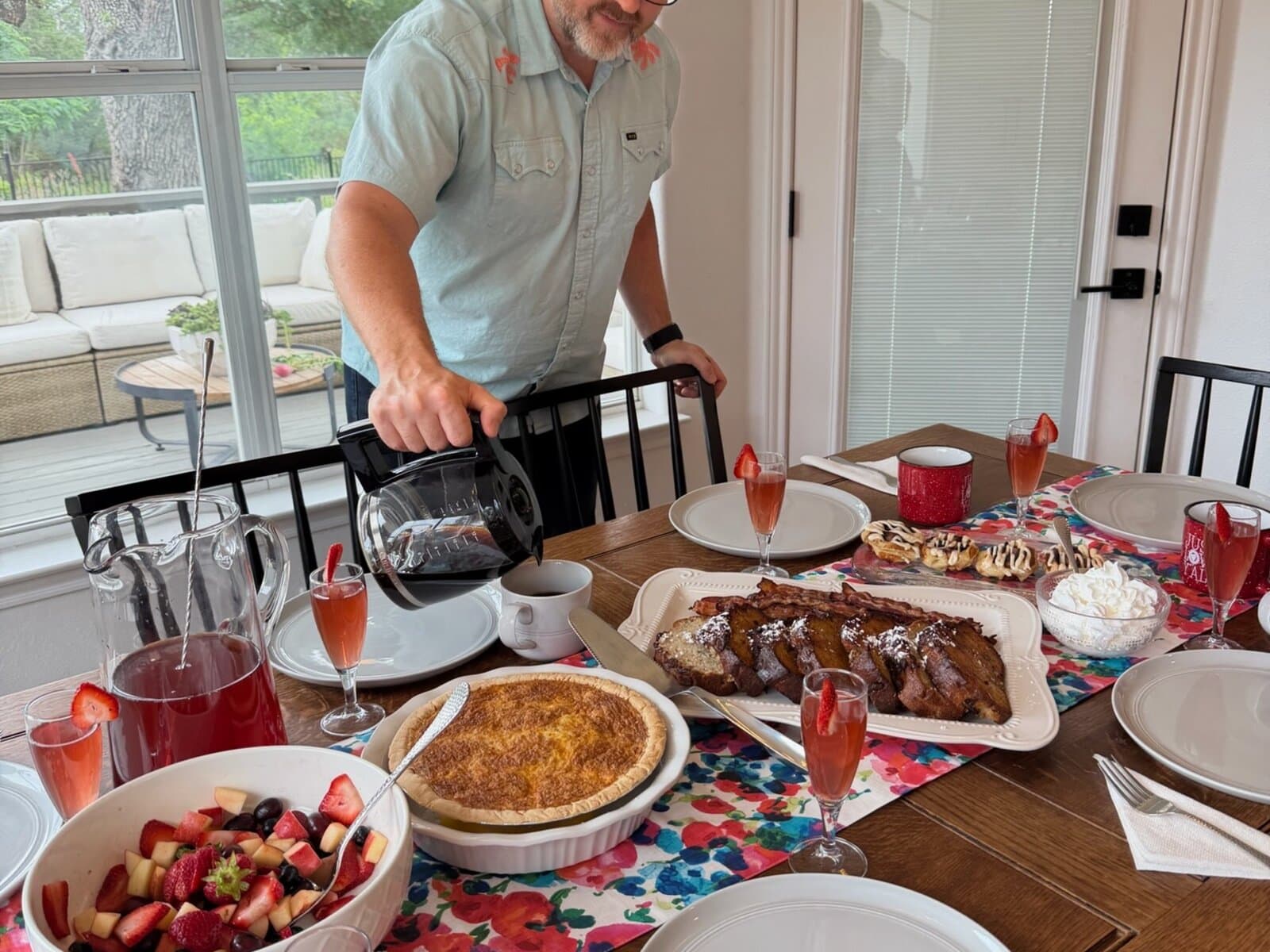 Dad pouring coffee over a full Mother's Day brunch table with quiche, fruit, and mocktails