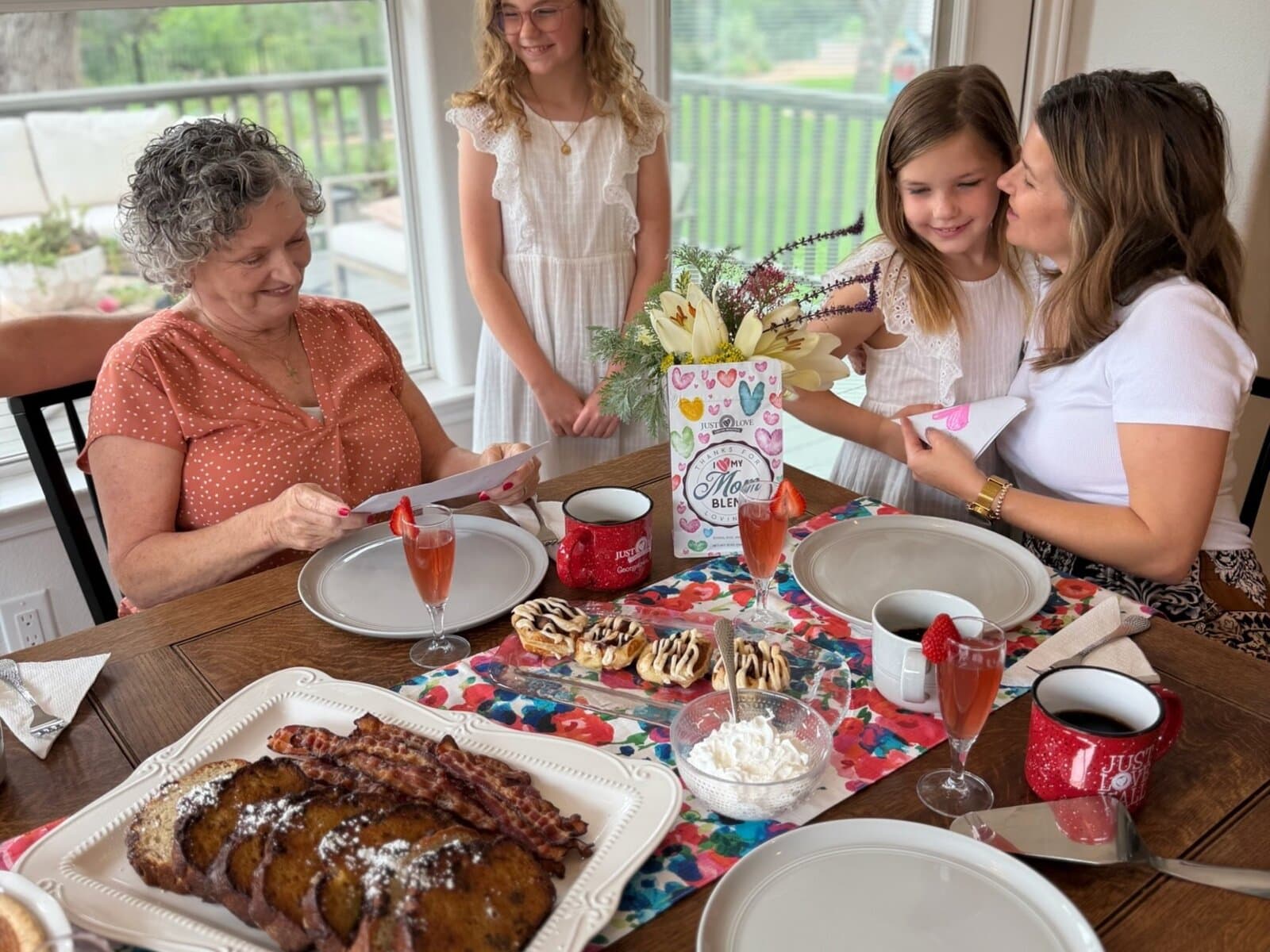 Three generations sharing a Mother's Day brunch table with French toast, bacon, and quiche